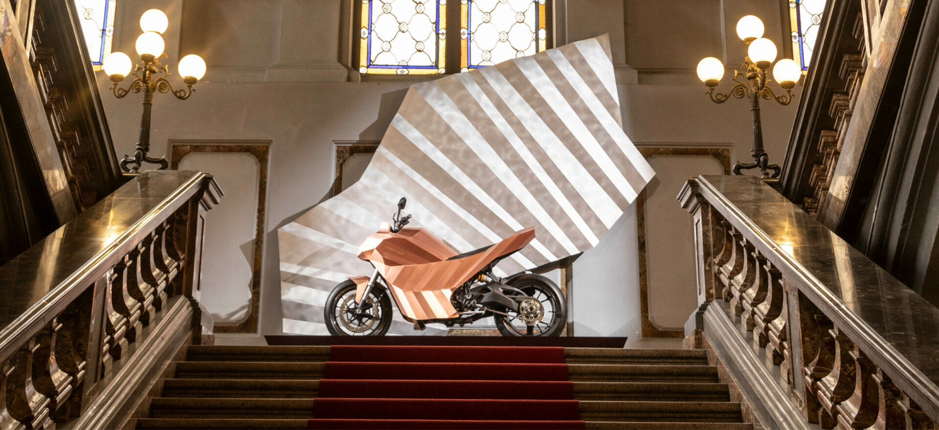 Left side of a standalone copper motorbike built on a Ducati Monster chassis on a quarter landing inside of Litta Palace of Milan, Italy.