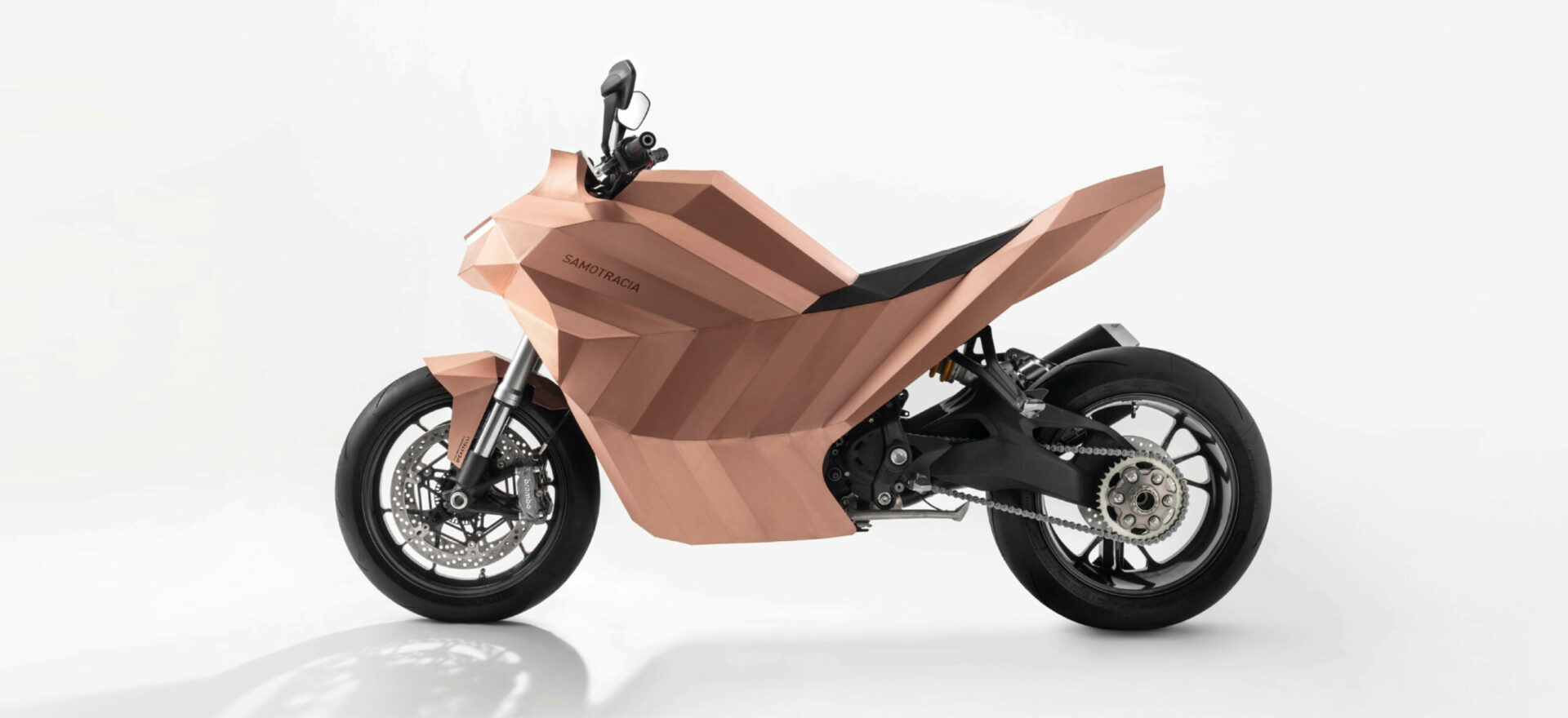 Left side of a standalone copper motorbike built on a Ducati Monster chassis in a white background.