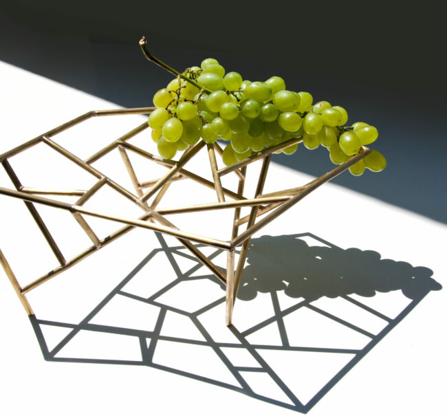 Oggetti Smarritti center piece by Mario Trimarchi holding grapes showing a projection of shadows on the table in an architectural style.