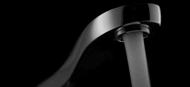 Close up picture of the Swan Kitchen faucet with water coming from the hose in a black background. The design was awarded the Good Design Award in 2017.